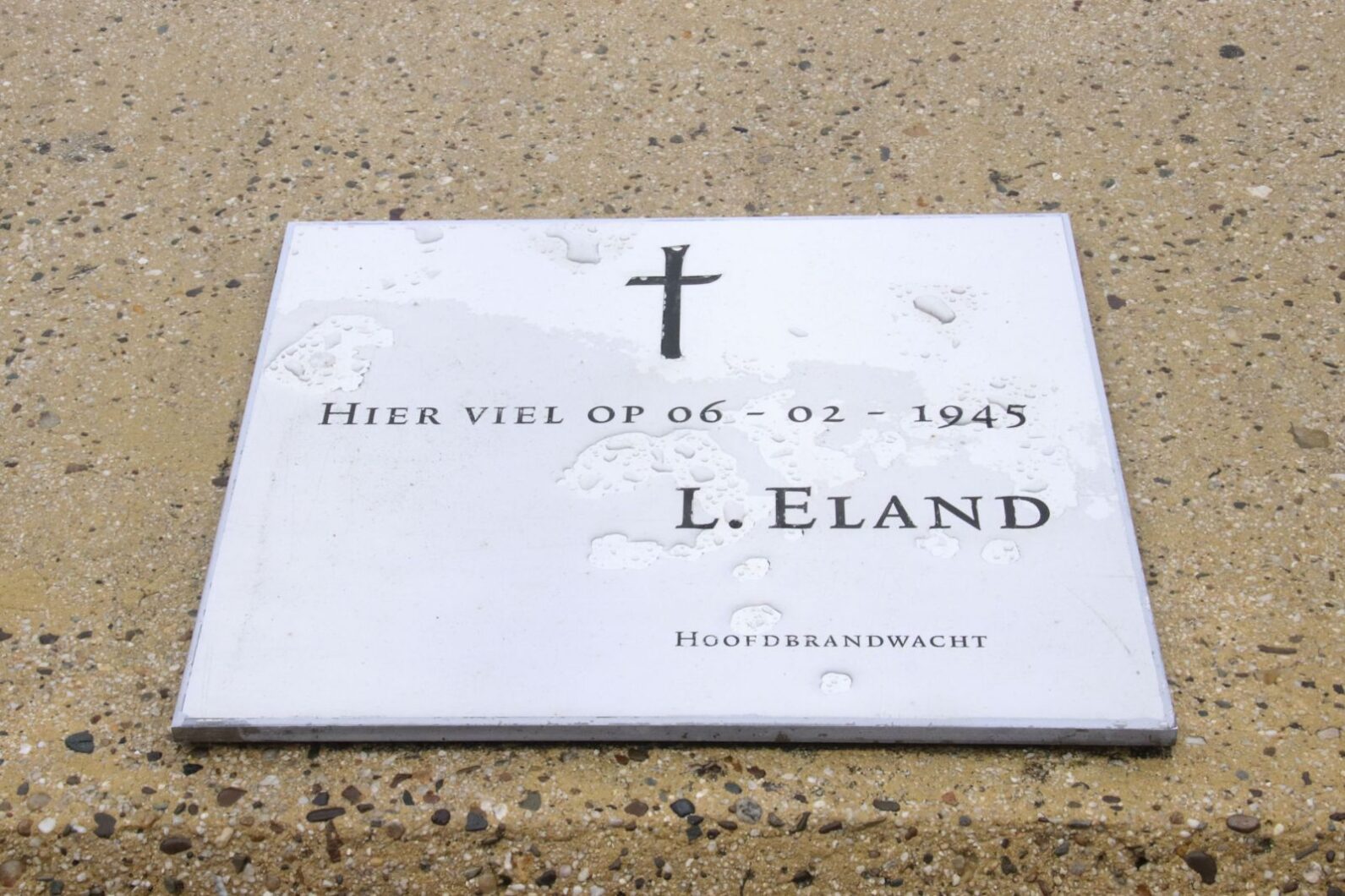 Herdenkingsplaquette RVS / Herdenkingsmonument Een tegel met de tekst: “Hier viel op 06-02-1945, L. Eland, hoofdbrandwacht”. Ook is er een beugel van de vlaggenmast aanwezig.